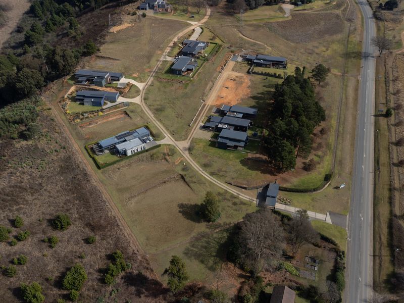 An aerial view of a residential estate featuring multiple modern dwellings, internal access roads, and surrounding natural landscape.