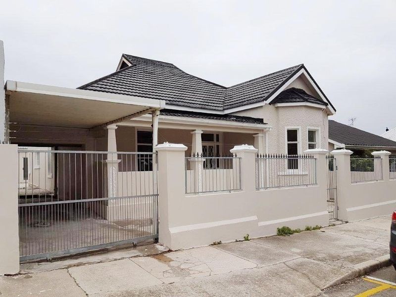 Front exterior view of a residential property featuring a tiled roof, a covered carport, and a secure perimeter wall with metal fencing and gate.