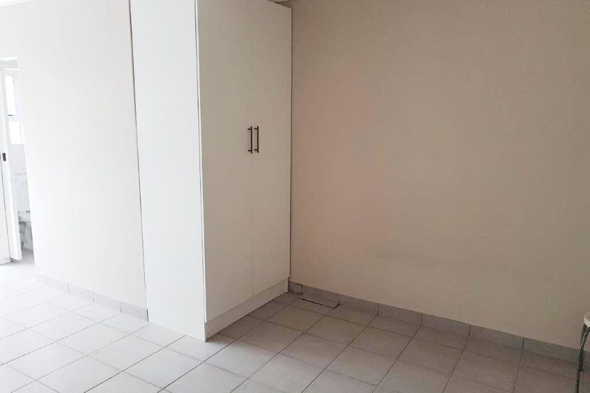 A clean, empty bedroom featuring neutral walls, tiled flooring, and a white built-in wardrobe.