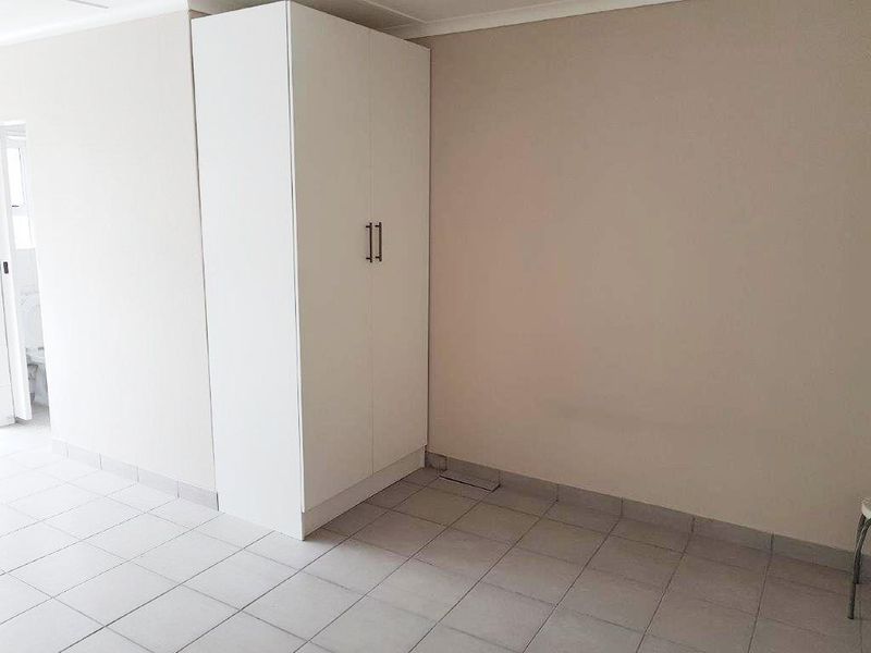 A clean, empty bedroom featuring neutral walls, tiled flooring, and a white built-in wardrobe.