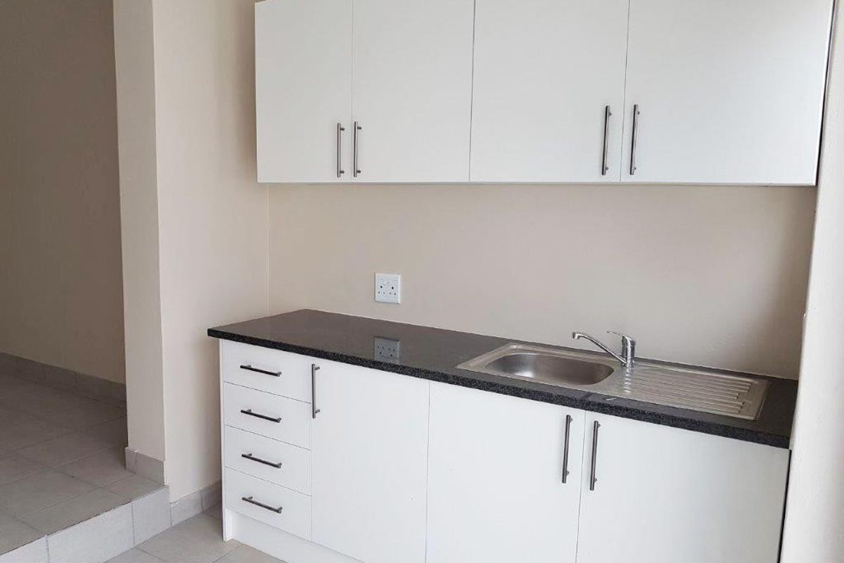 A clean, functional kitchen area featuring white cabinetry, dark granite countertops, and a stainless steel sink with a modern mixer tap.