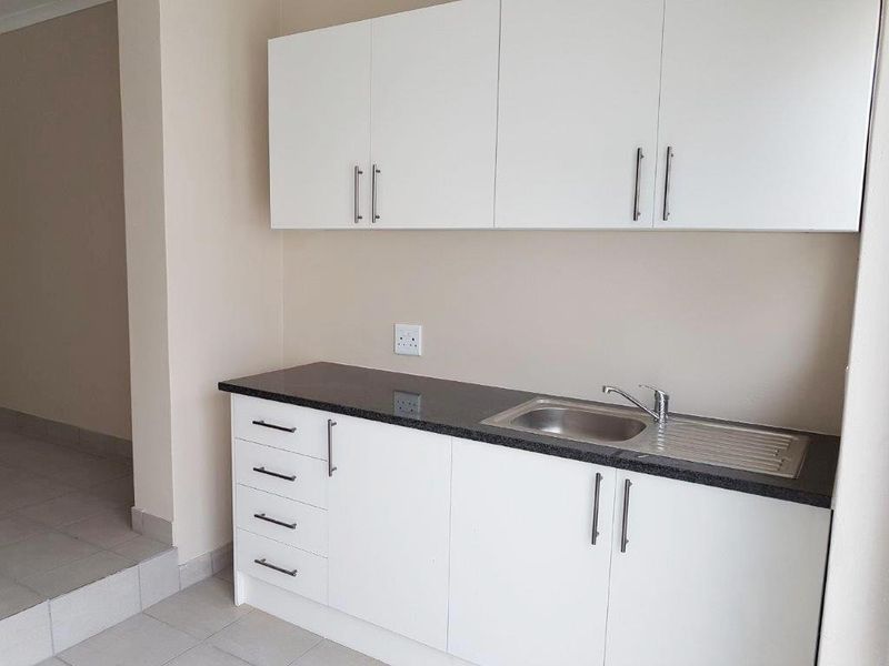A clean, functional kitchen area featuring white cabinetry, dark granite countertops, and a stainless steel sink with a modern mixer tap.