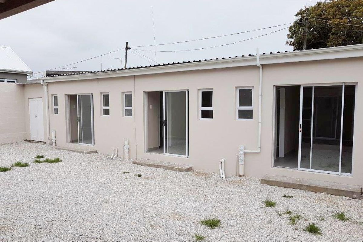 Rear exterior view of the apartment building featuring multiple sliding glass door access points and a gravel courtyard area.