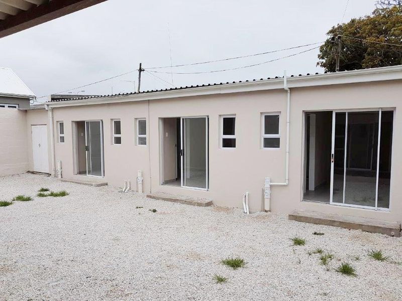 Rear exterior view of the apartment building featuring multiple sliding glass door access points and a gravel courtyard area.