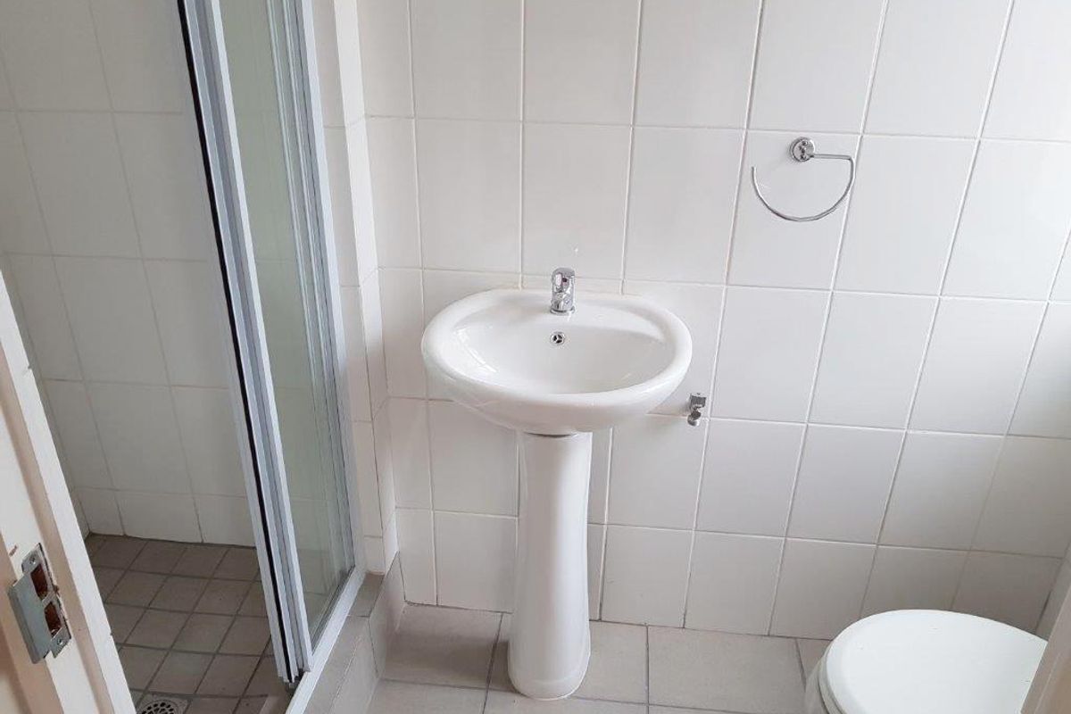 A functional bathroom featuring a pedestal basin, shower enclosure, and tiled finishes, presenting a clean but dated aesthetic suitable for modernization.