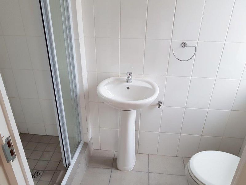 A functional bathroom featuring a pedestal basin, shower enclosure, and tiled finishes, presenting a clean but dated aesthetic suitable for modernization.