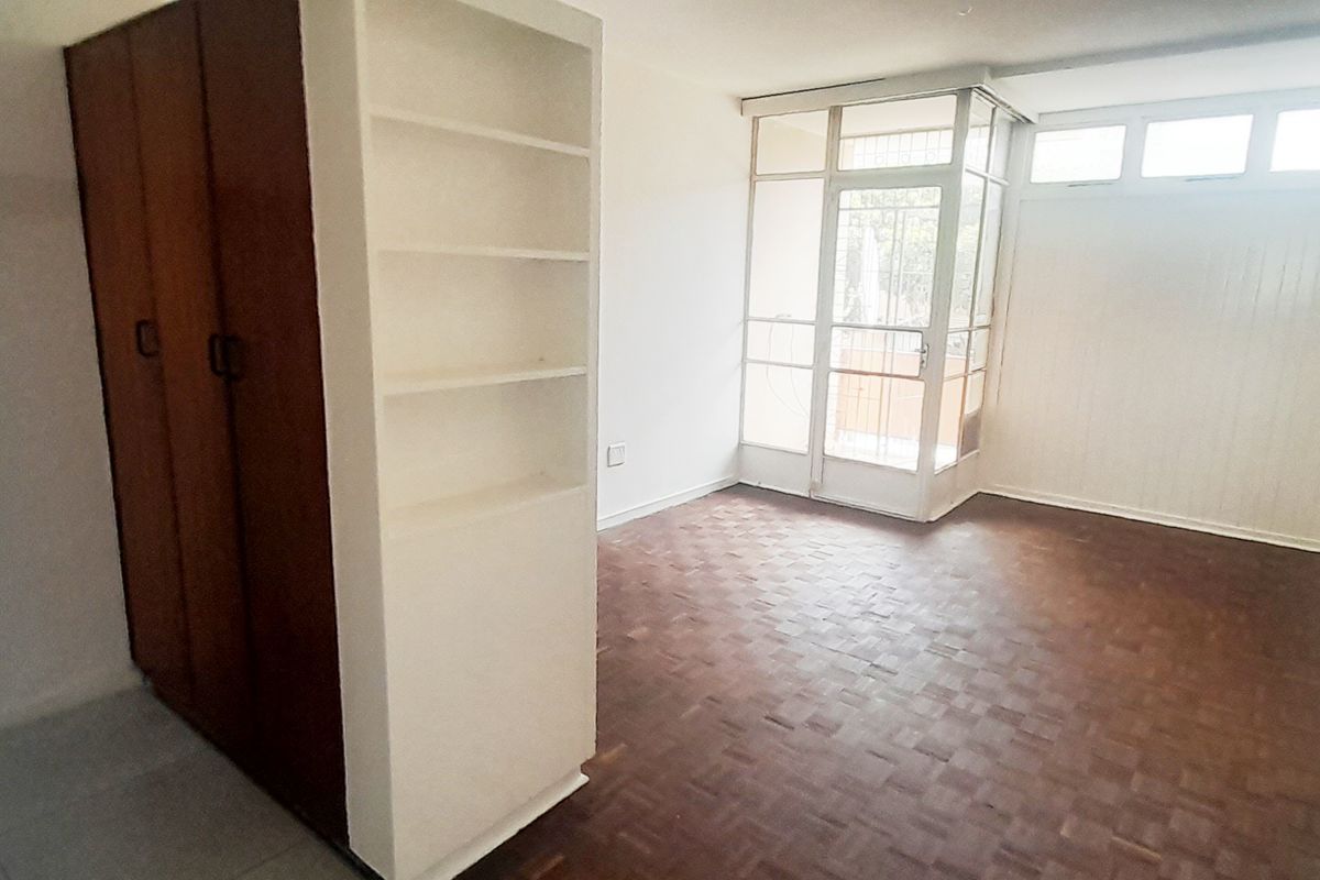 Empty bedroom featuring parquet flooring, built-in wardrobe, and built-in shelving, with direct access to an enclosed balcony area.