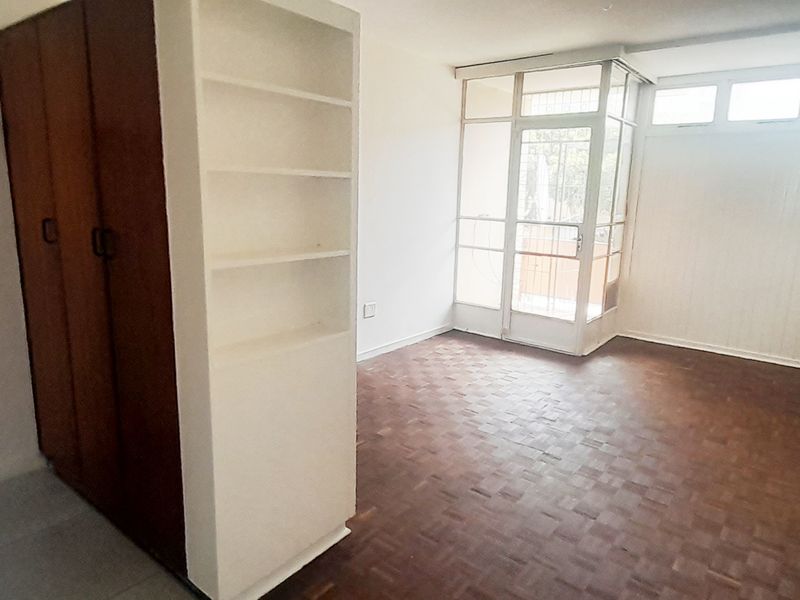 Empty bedroom featuring parquet flooring, built-in wardrobe, and built-in shelving, with direct access to an enclosed balcony area.