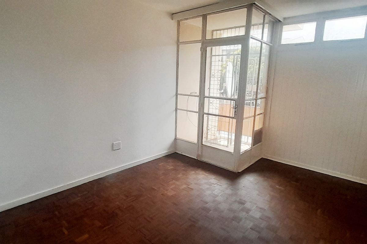 An empty living room featuring original parquet flooring and direct access to an enclosed balcony through a glass-paneled door.