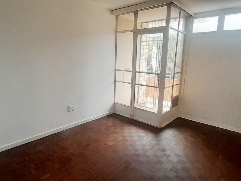 An empty living room featuring original parquet flooring and direct access to an enclosed balcony through a glass-paneled door.