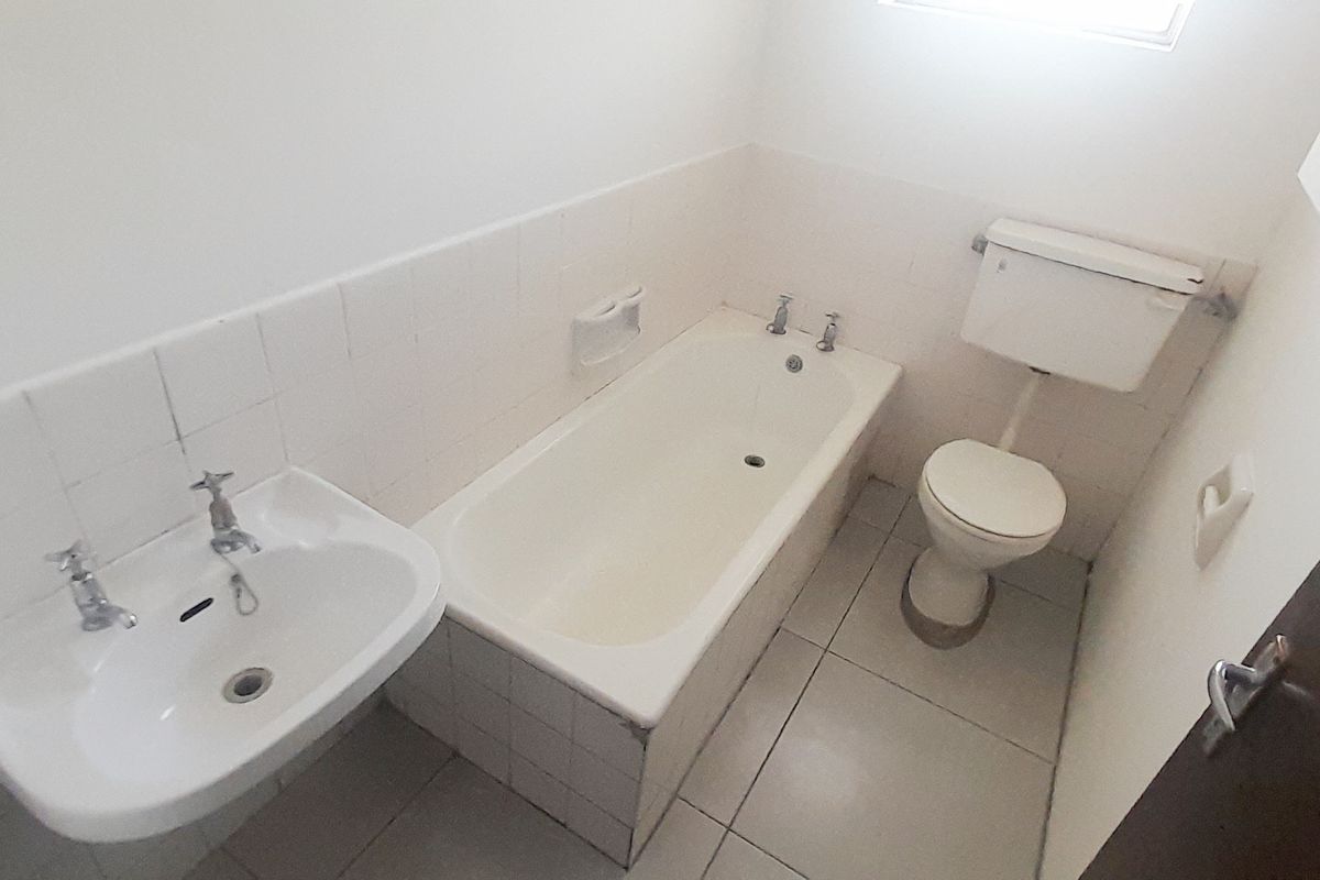 A functional bathroom featuring a standard bathtub, pedestal basin, and toilet with tiled finishes, presenting an opportunity for modernization and cosmetic updates.