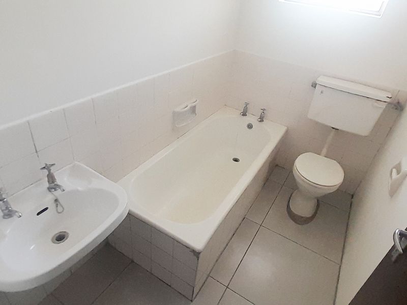 A functional bathroom featuring a standard bathtub, pedestal basin, and toilet with tiled finishes, presenting an opportunity for modernization and cosmetic updates.