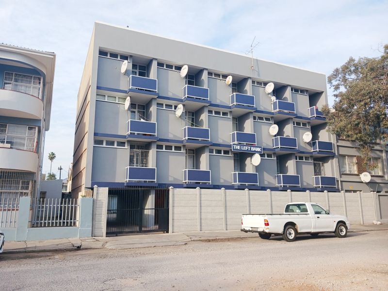 Exterior view of The Left Bank apartment building featuring multiple balconies, a secure gated entrance, and perimeter walling.