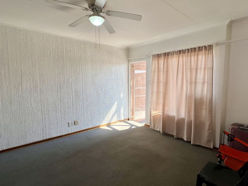 A bright, empty living room featuring textured walls, a ceiling fan, and direct access to an outdoor area through a sliding glass door.