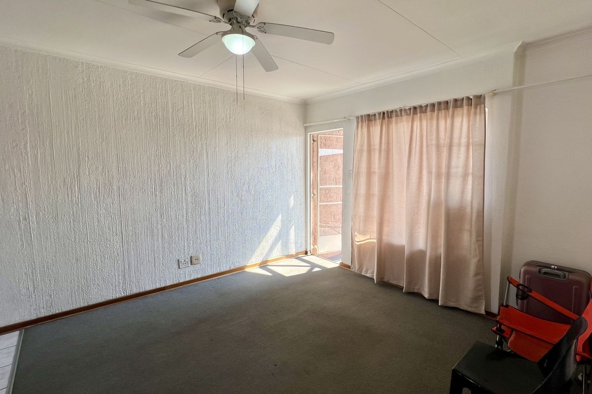 A bright, empty living room featuring textured walls, a ceiling fan, and direct access to an outdoor area through a sliding glass door.