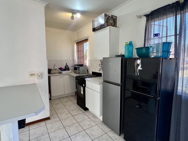 Compact kitchen featuring tiled flooring, built-in cabinetry, a stainless steel sink, and a freestanding stove with a tiled backsplash.