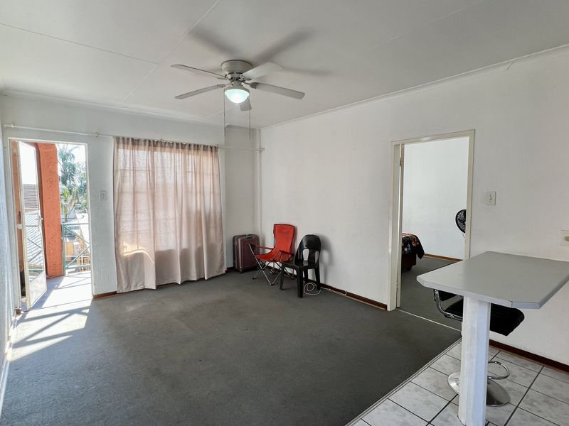 Open plan living area featuring a breakfast bar, ceiling fan, and direct access to a balcony, with neutral finishes throughout.