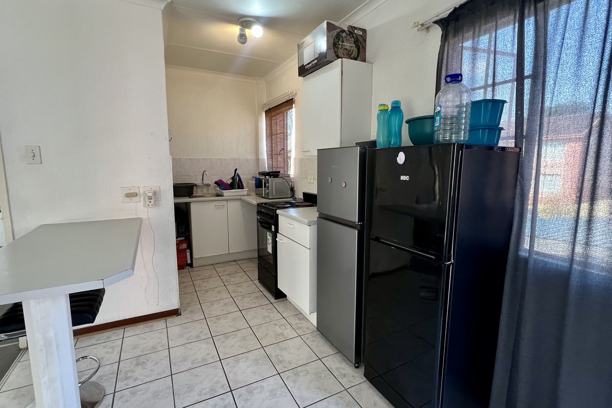 A functional kitchen featuring tiled flooring, built-in cabinetry, a stainless steel sink, and a breakfast counter, offering potential for modernization.