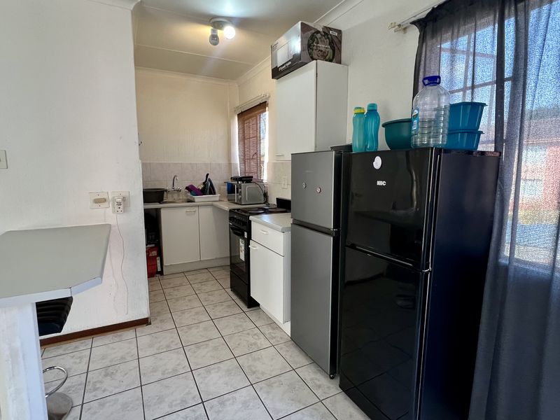 A functional kitchen featuring tiled flooring, built-in cabinetry, a stainless steel sink, and a breakfast counter, offering potential for modernization.