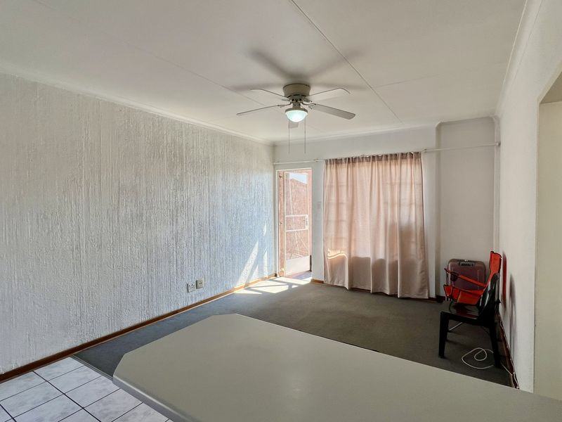 Open plan living area featuring a textured feature wall, ceiling fan, and a mix of tiled and carpeted flooring with access to an outdoor area.