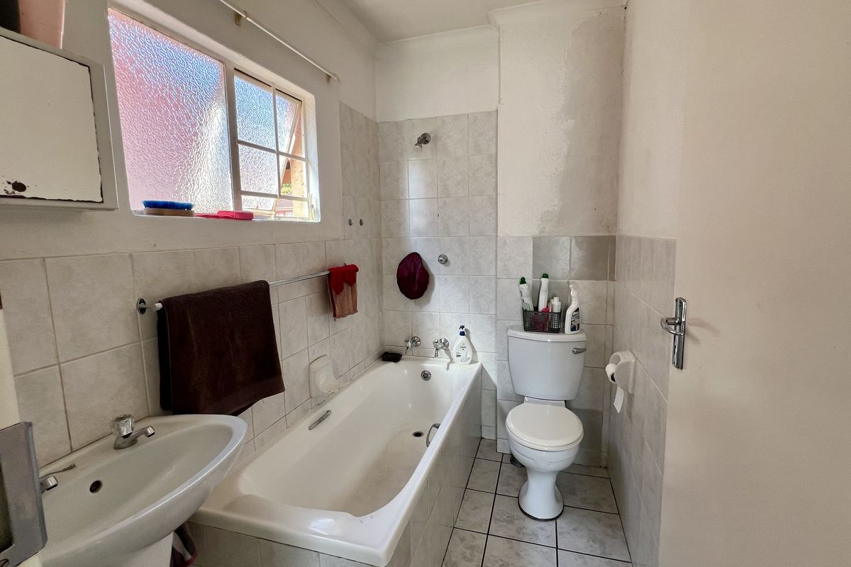 A dated bathroom featuring a standard bathtub, pedestal basin, and toilet with tiled finishes, requiring cosmetic updates and maintenance to the wall surfaces.