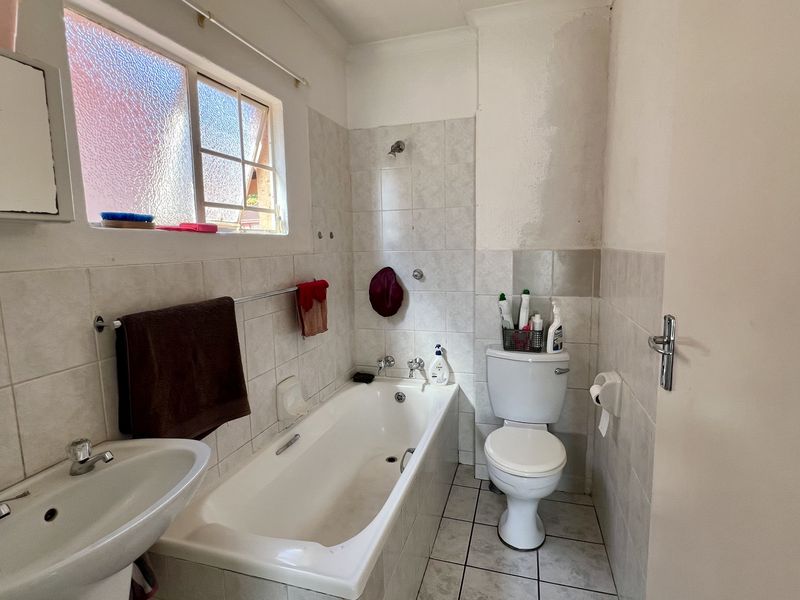 A dated bathroom featuring a standard bathtub, pedestal basin, and toilet with tiled finishes, requiring cosmetic updates and maintenance to the wall surfaces.