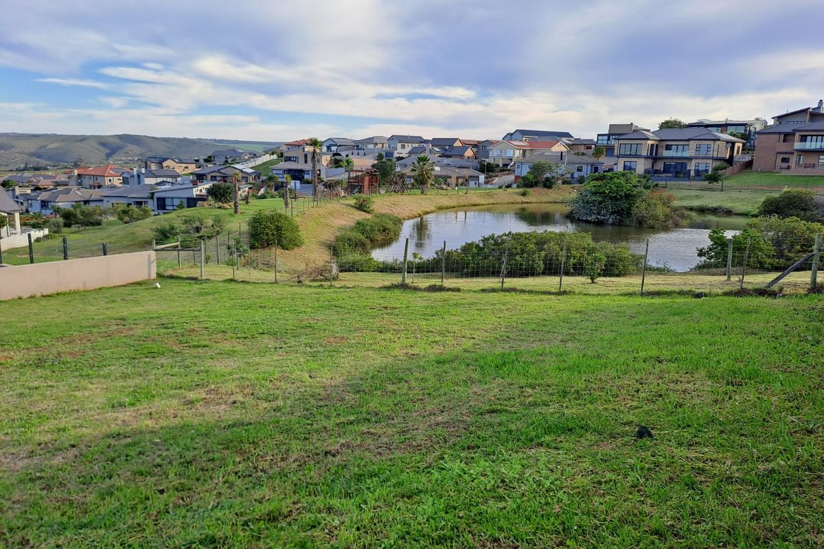 A scenic view of a residential estate featuring a landscaped pond, green lawn, and surrounding suburban homes.
