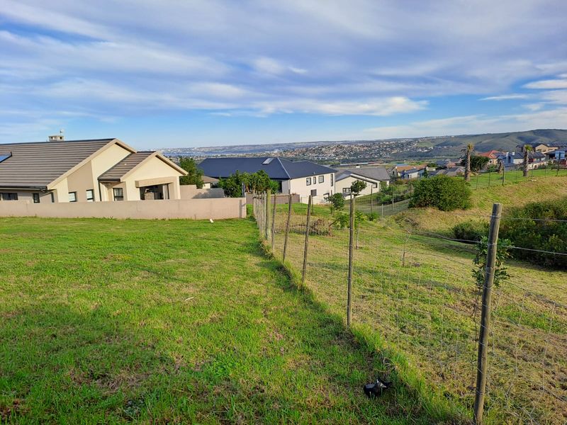 A view of a vacant residential plot featuring a grass lawn and wire mesh fencing, overlooking a suburban neighborhood.