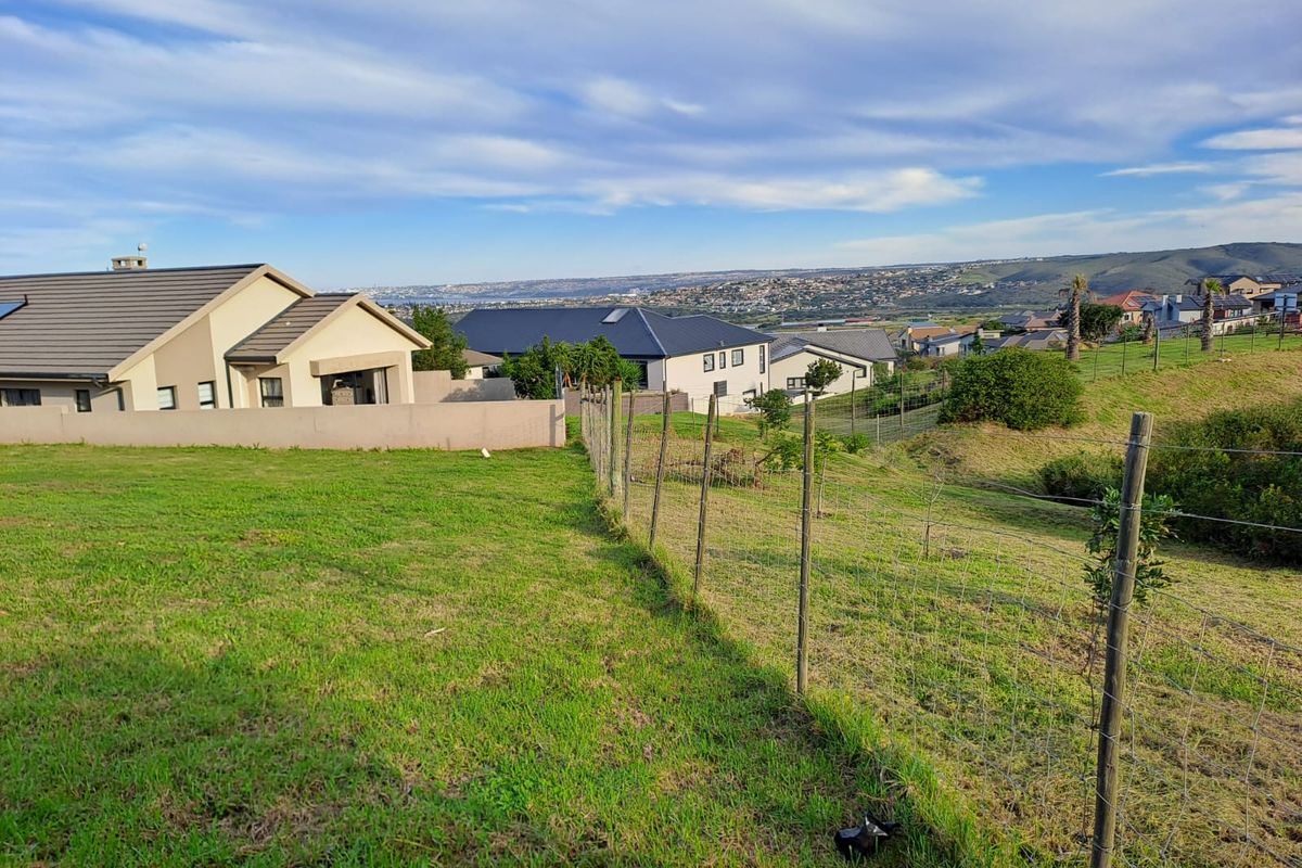 A view of a vacant residential plot featuring a grass lawn and wire mesh fencing, overlooking a suburban neighborhood.