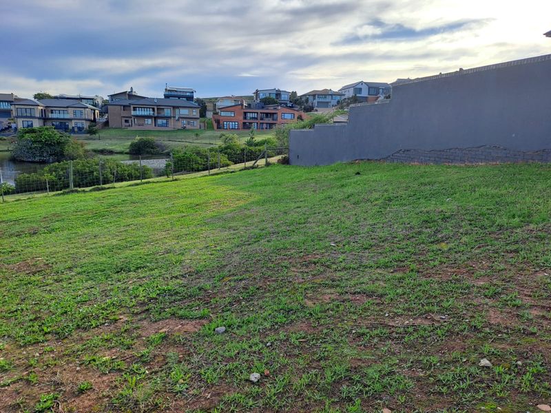 A vacant residential plot featuring a grassed area, wire fencing, and a retaining wall with visible masonry cracks, overlooking a suburban landscape.