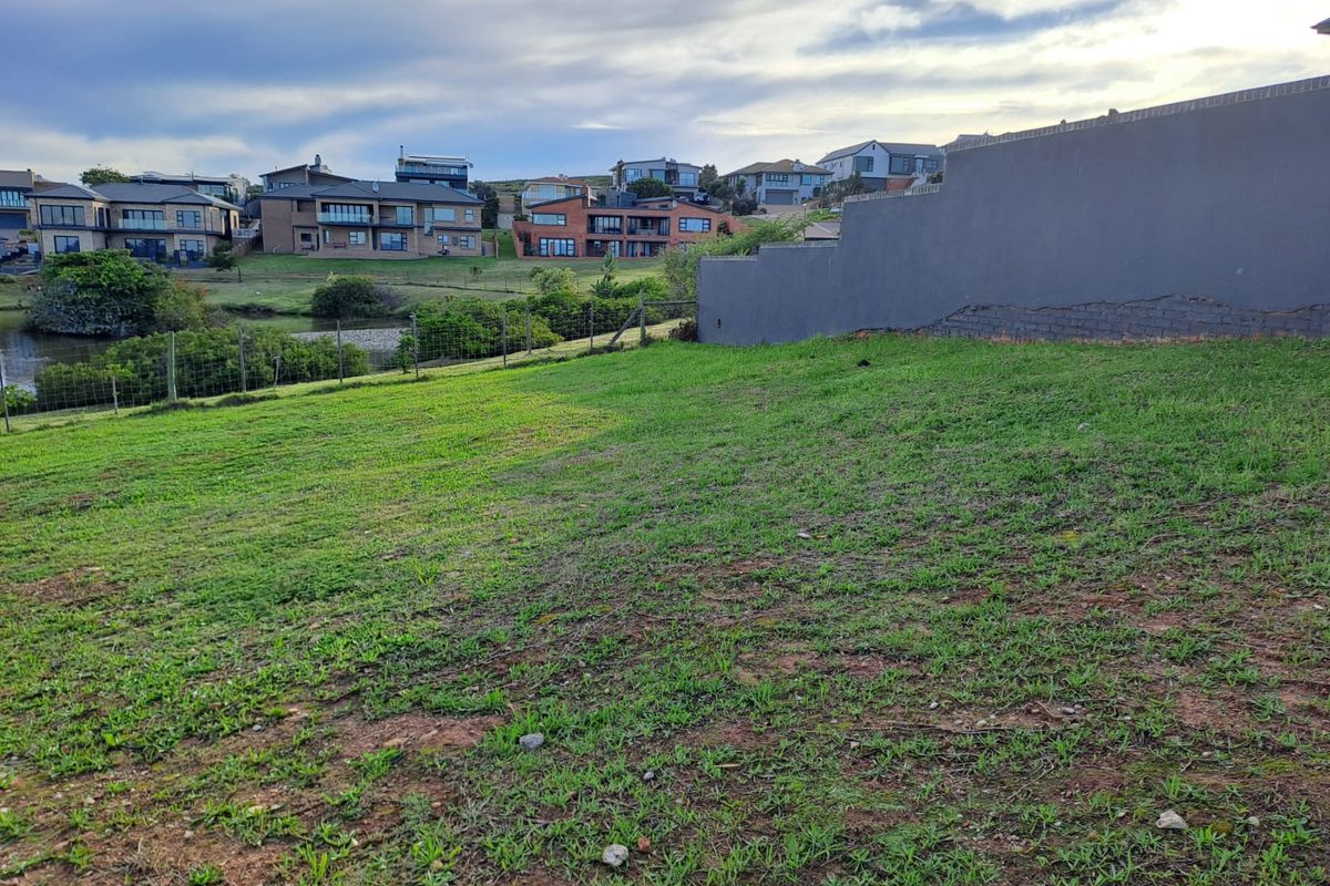 A vacant residential plot featuring a grassed area, wire fencing, and a retaining wall with visible masonry cracks, overlooking a suburban landscape.