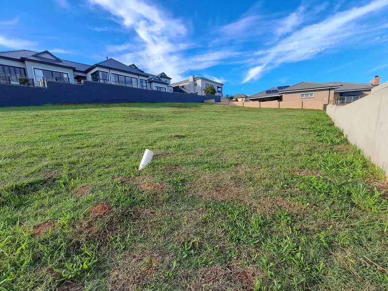 A vacant residential plot featuring a gentle slope, established grass, and surrounding boundary walls in a developed neighborhood.
