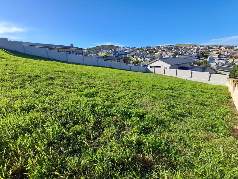 A view of the vacant residential land plot featuring a sloped grass surface and established boundary walls, overlooking the surrounding neighborhood.