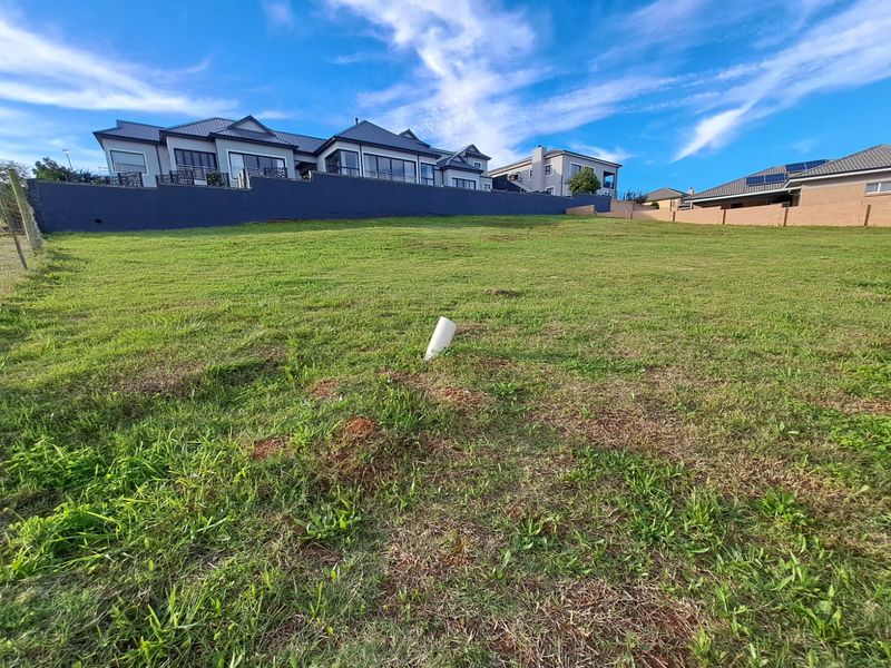 A vacant residential plot featuring a gentle slope, established grass, and a retaining wall bordering the neighboring property.
