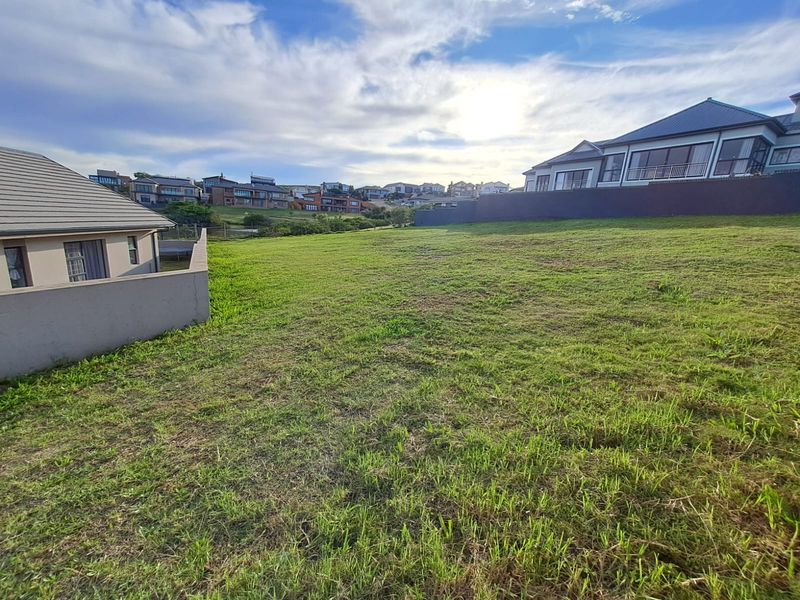 A vacant residential plot featuring a grass lawn and boundary wall, situated in a developed neighborhood with surrounding residential properties.