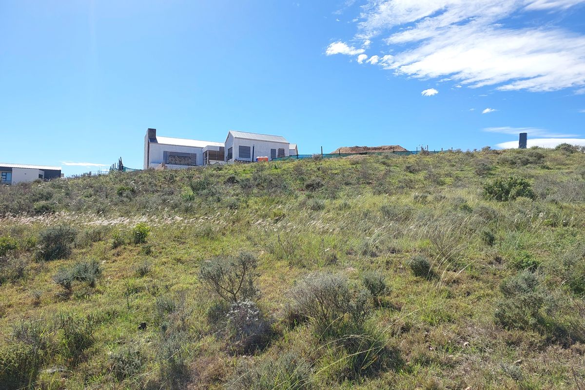 A view of the sloped residential land featuring native vegetation and surrounding fencing, with neighboring structures visible in the distance.