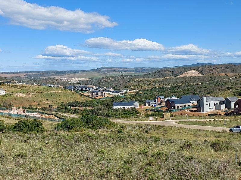 An elevated view of a vacant residential plot overlooking a developing estate with surrounding hills and natural landscape.