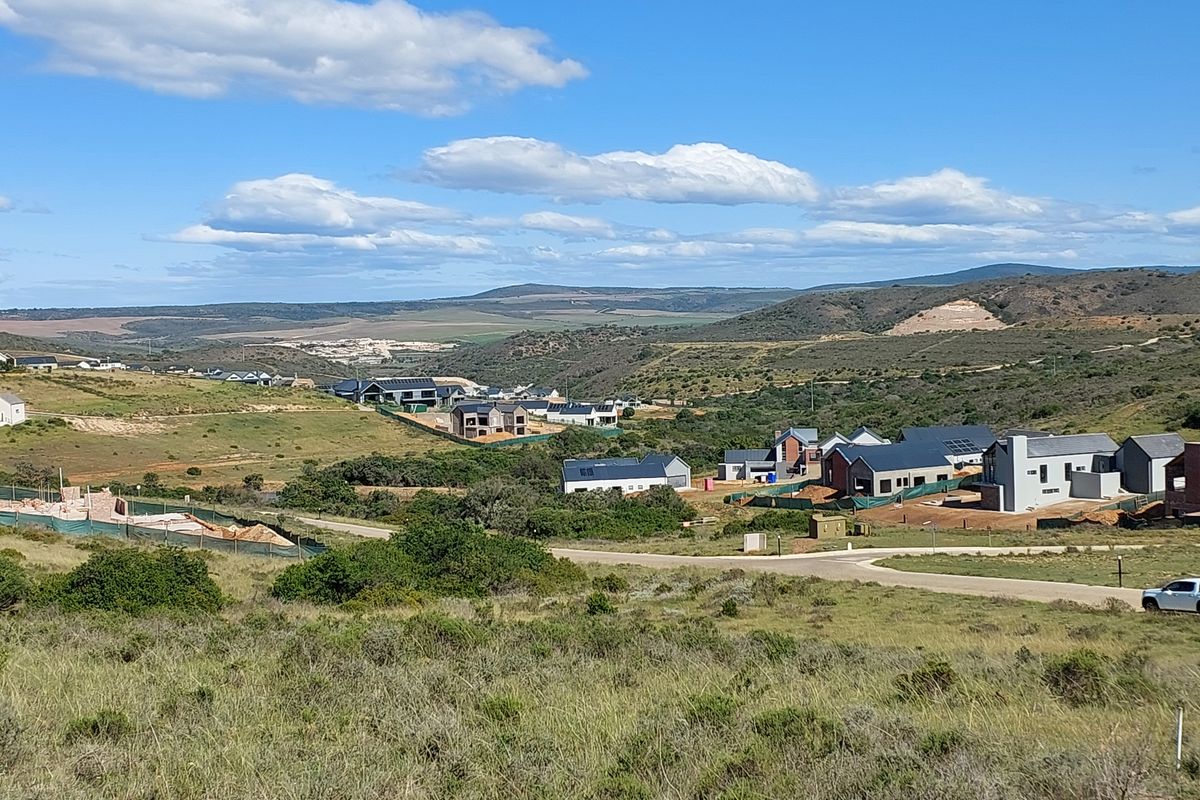 An elevated view of a vacant residential plot overlooking a developing estate with surrounding hills and natural landscape.