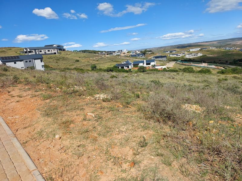 An elevated view of a vacant residential plot overlooking a developing estate with surrounding hillside landscape and neighbouring modern homes.