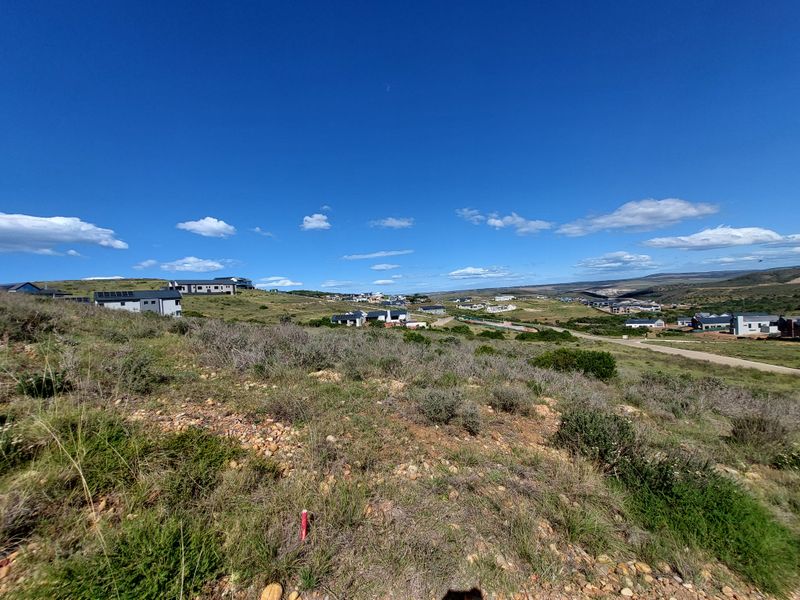 A wide-angle view of the vacant residential land, showcasing the natural sloped terrain and surrounding neighborhood landscape under a clear blue sky.