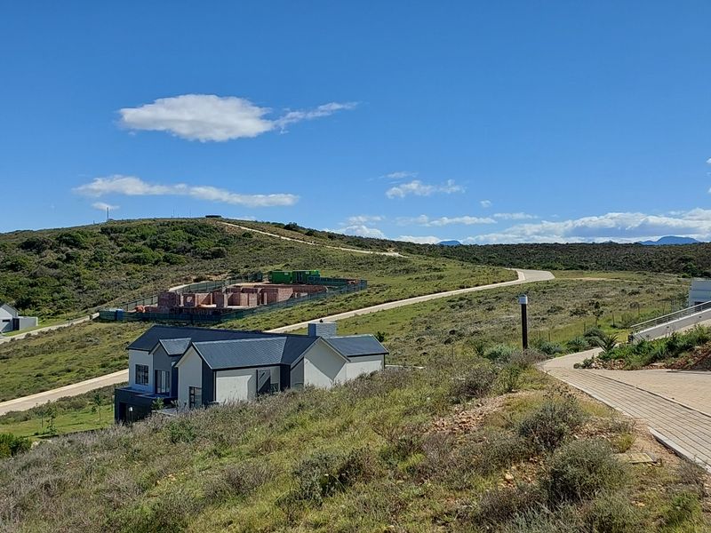 An elevated view of a residential property under development, featuring a modern home with a pitched roof set within a scenic landscape.