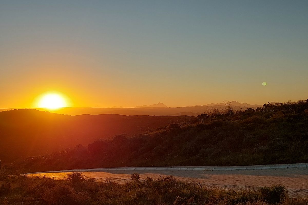 A scenic sunset view overlooking rolling hills and distant mountains from a paved residential road.