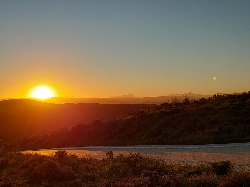 A scenic sunset view overlooking rolling hills and distant mountains from a paved residential road.
