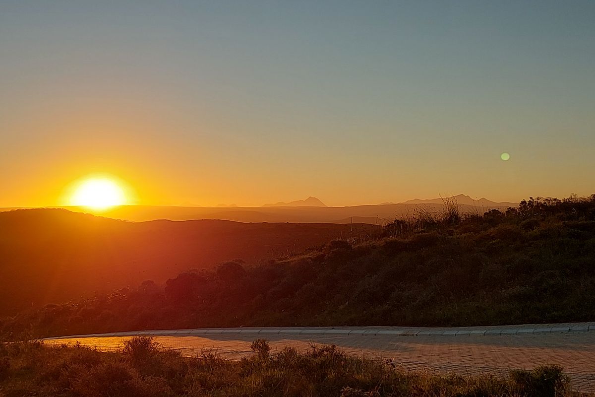 A scenic sunset view overlooking rolling hills and distant mountains, featuring a paved road in the foreground of this vacant residential land.