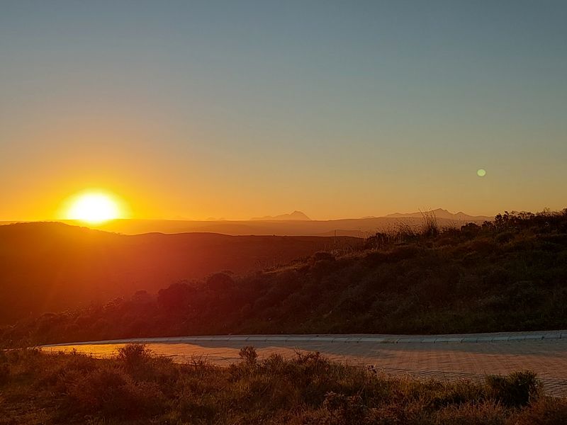 A scenic sunset view overlooking rolling hills and distant mountains, featuring a paved road in the foreground of this vacant residential land.