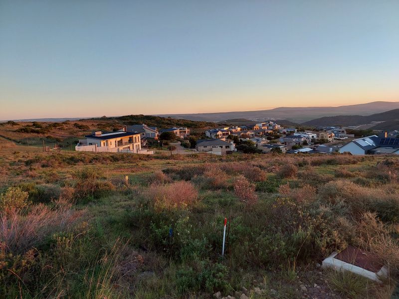 Elevated view overlooking a residential estate with natural landscape in the foreground and surrounding hills at sunset.