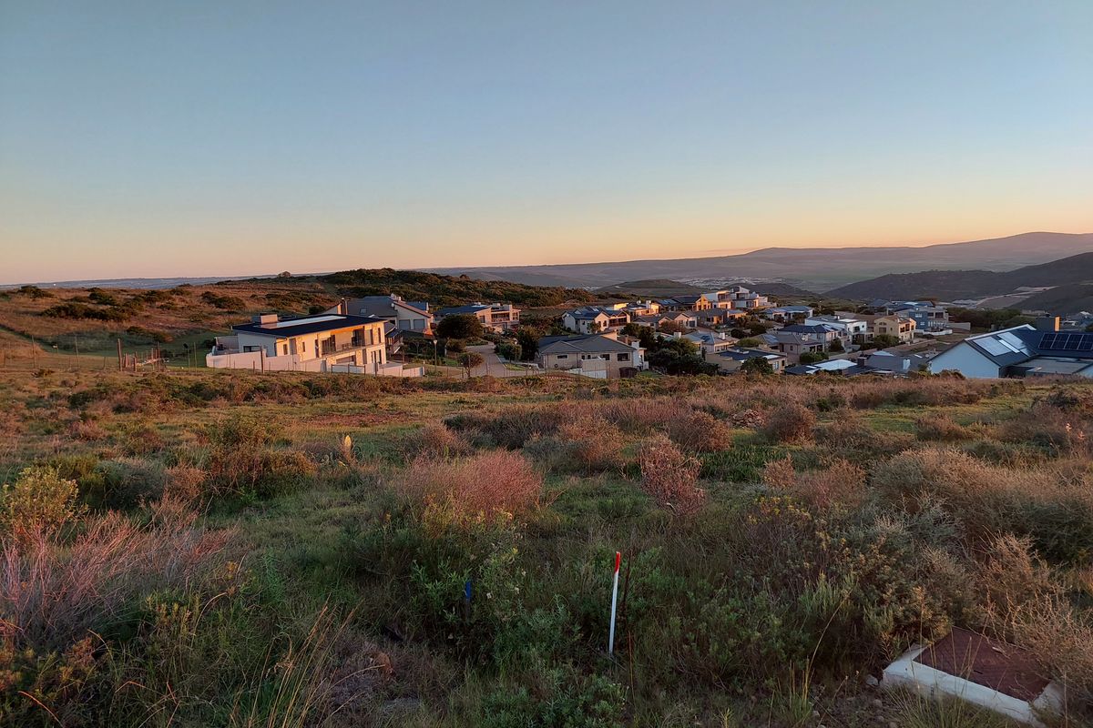 Elevated view overlooking a residential estate with natural landscape in the foreground and surrounding hills at sunset.