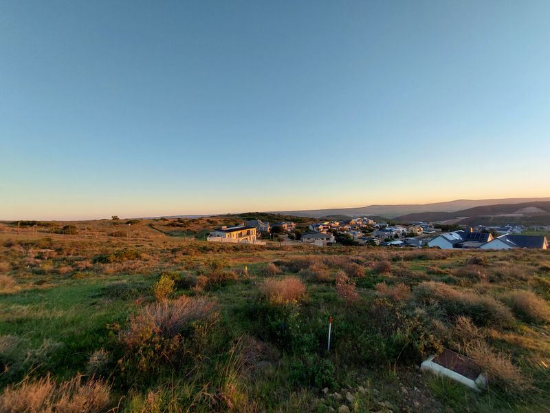 A wide-angle view of the vacant residential land, showcasing the surrounding landscape and nearby neighborhood development at sunset.