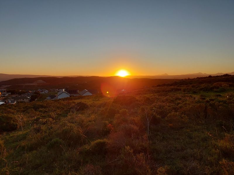 A scenic sunset view overlooking the surrounding landscape and distant residential area, showcasing the natural beauty of the vacant land.