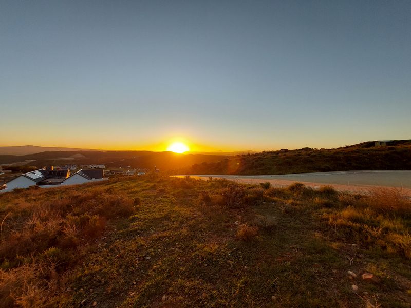 A scenic sunset view overlooking the surrounding landscape and residential area from the vacant residential plot.